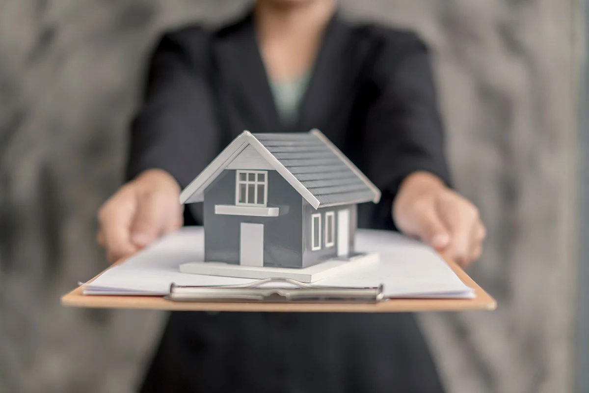 Agent holding a model house above signed paperwork