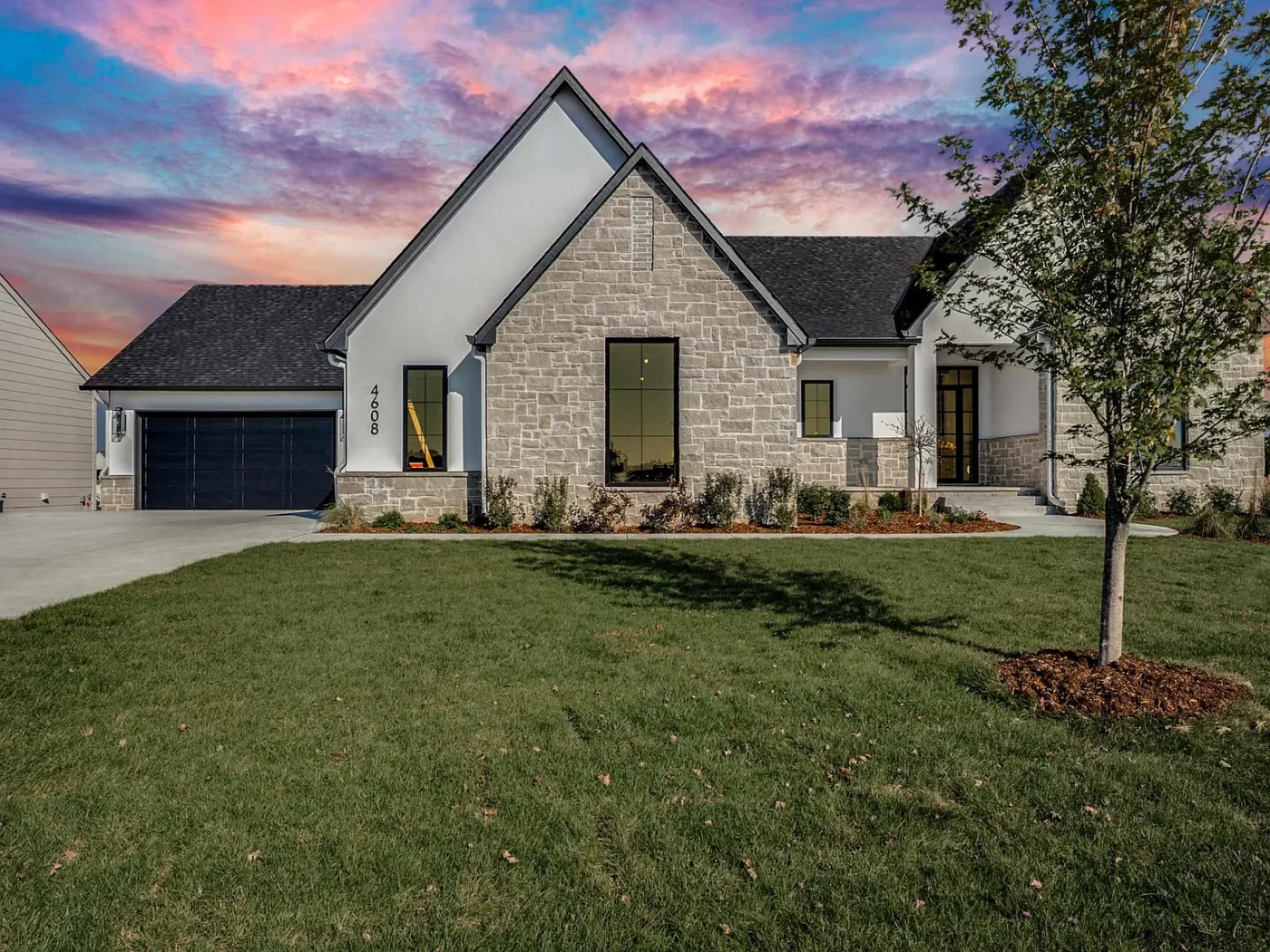 Sharp Homes house at The Reber at dusk, in light coursed stone with white stucco gables and black windows